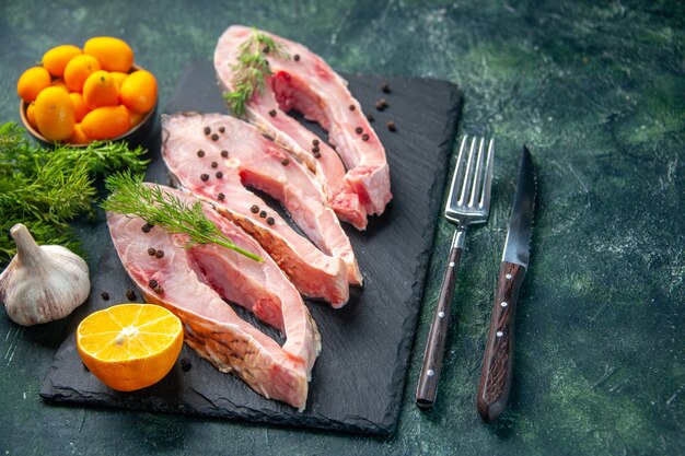 Vista frontal rebanadas de pescado fresco con verduras y kumquats en la superficie oscura carne del océano comida cruda foto de agua cena de color de mariscos