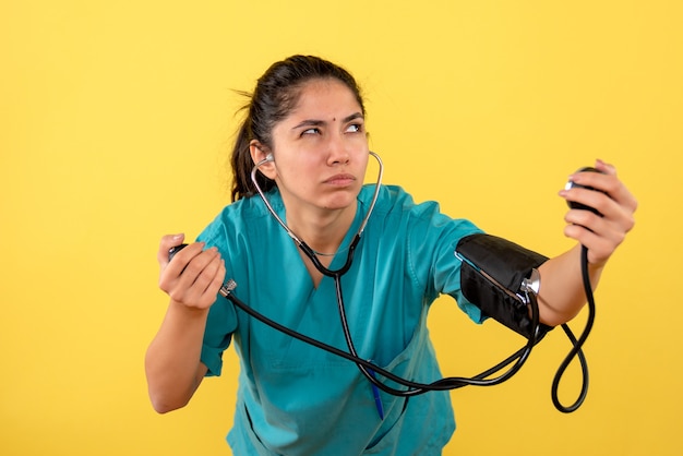 Vista frontal reflexiva joven doctora con esfigmomanómetro sobre fondo amarillo