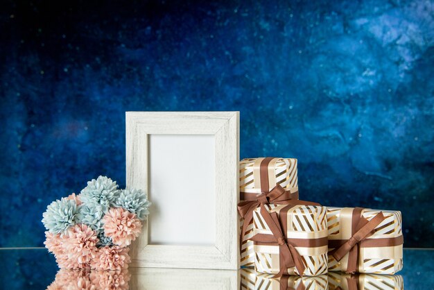 Vista frontal regalos del día de san valentín flores marco de fotos blanco reflejado en el espejo sobre fondo azul oscuro
