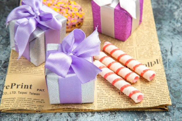 Vista frontal regalos de Navidad galletas de colores en el periódico sobre fondo gris aislado