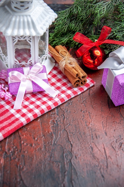 Vista frontal regalos de navidad ramas de árboles de pino bola de navidad linterna de juguete mantel rojo palitos de canela sobre fondo rojo oscuro foto de navidad