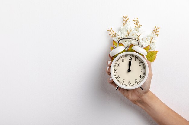 Vista frontal del reloj en la mano con hojas y flores.
