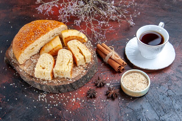 Vista frontal de repostería dulce en rodajas en trozos con una taza de té sobre fondo oscuro