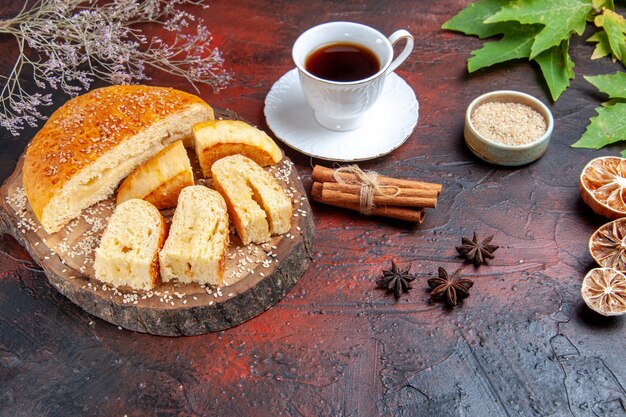 Vista frontal de repostería dulce en rodajas en trozos con una taza de té sobre fondo oscuro