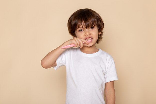 Vista frontal del retrato, chico lindo adorable en camiseta blanca sobre escritorio rosa