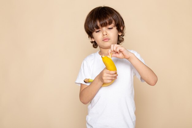 Vista frontal del retrato, niño pequeño adorable adorable en camiseta blanca con pared rosa bananon