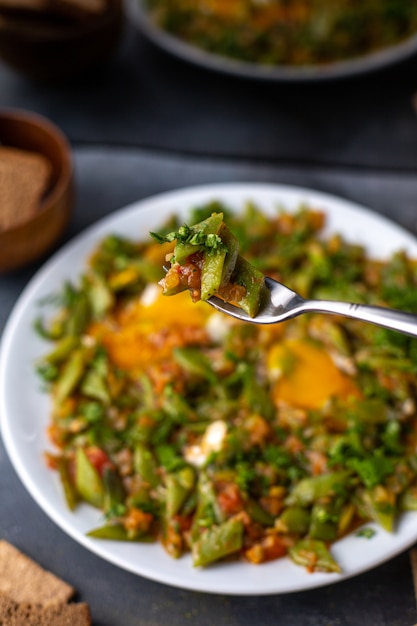 Una vista frontal en rodajas comida de vegetales sabroso colorido dentro de un plato blanco junto con huevos crujientes en la mesa gris plato verduras
