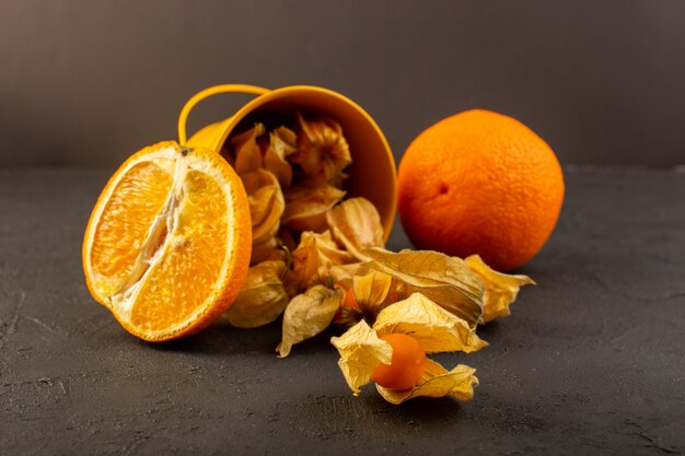 Una vista frontal en rodajas de naranjas junto con frutas redondas naranjas peladas extendidas en gris