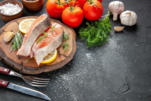 Vista frontal de las rodajas de pescado fresco con rodajas de limón y tomates en la carne de color oscuro plato de mariscos foto de comida cruda