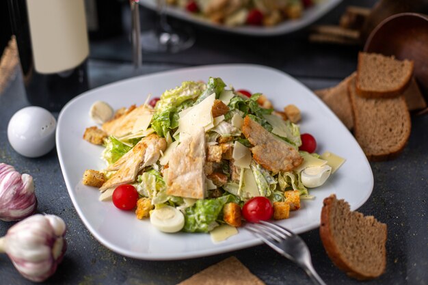 Una vista frontal en rodajas de pollo con verduras verdes dentro de un plato blanco salado, salpicado junto con patatas fritas de vino tinto en el escritorio gris platos de la cena