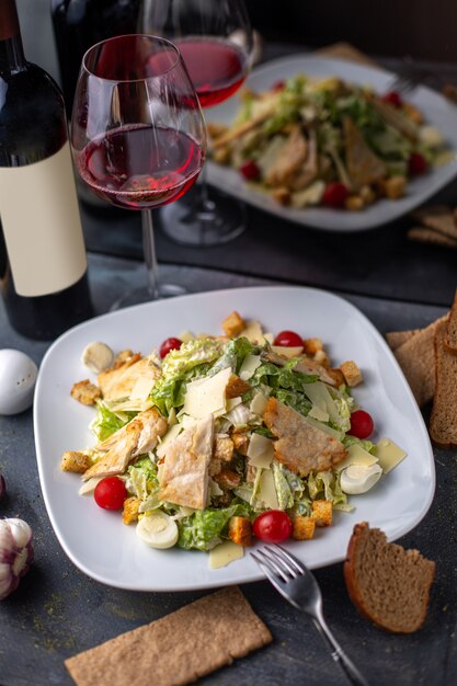 Una vista frontal en rodajas de pollo con verduras verdes dentro de un plato blanco salado, salpicado junto con patatas fritas de vino tinto en el escritorio gris platos de la cena