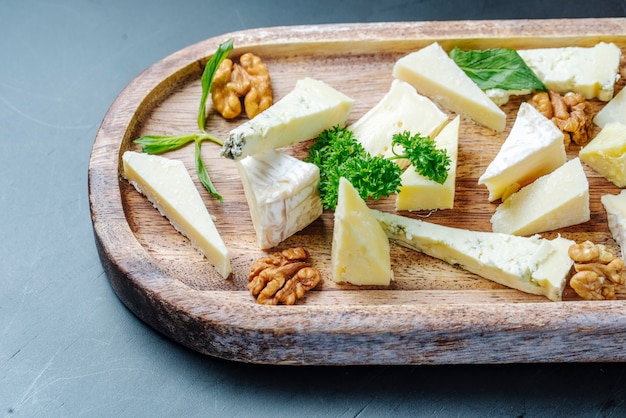 Vista frontal en rodajas de queso roquefort con verduras y nueces en un plato de madera