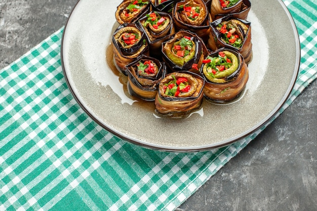 Vista frontal de rollos de berenjena rellenos en plato ovalado blanco mantel blanco turquesa sobre plato gris