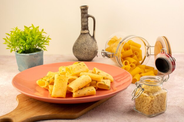 Vista frontal de una sabrosa comida de pasta italiana dentro de la placa rosa junto con flores y pasta cruda en rosa