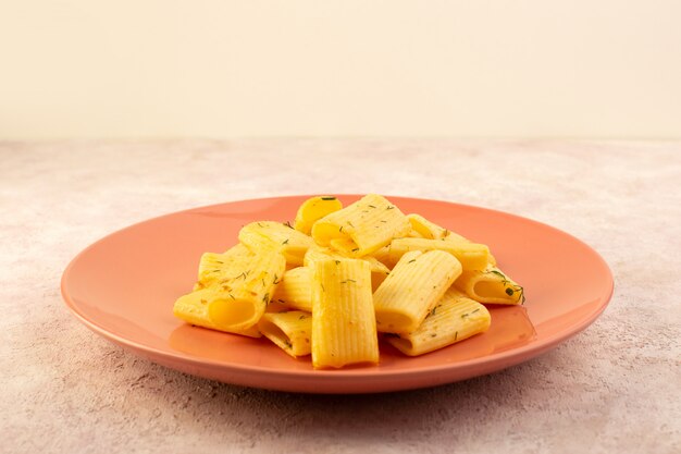 Vista frontal de una sabrosa comida de pasta italiana con hierbas verdes secas dentro de la placa rosa sobre rosa