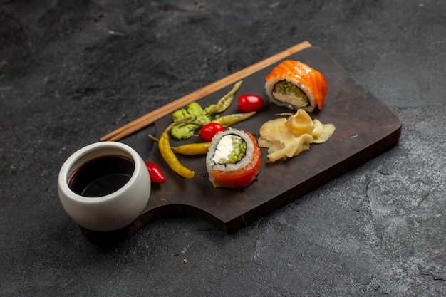 Vista frontal de la sabrosa comida de sushi en rodajas rollos de pescado con salsa en la pared gris