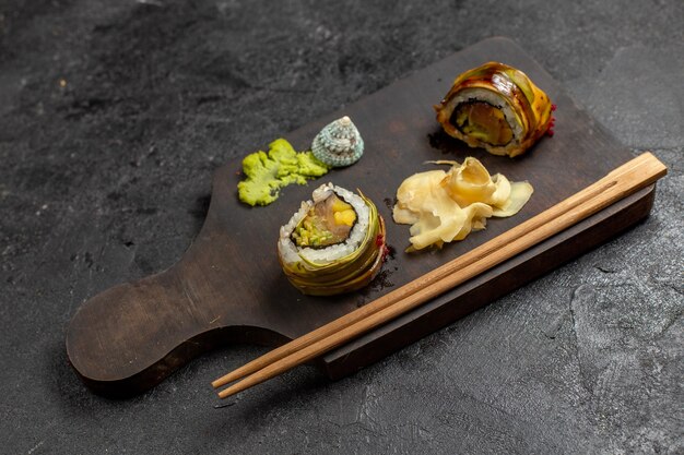 Vista frontal de la sabrosa comida de sushi en rodajas rollos de pescado con wassabi verde y palos en la pared gris