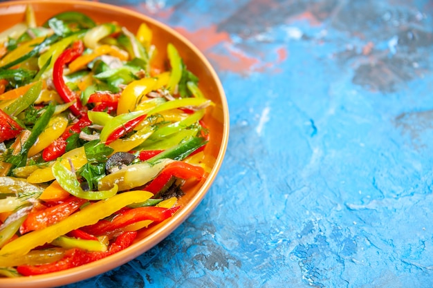 Vista frontal sabrosa ensalada de verduras dentro de la placa sobre la mesa azul