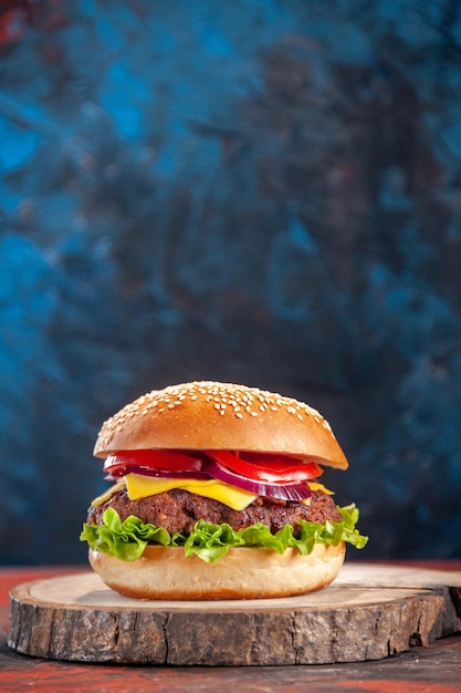 Vista frontal sabrosa hamburguesa con queso con carne, tomates y ensalada verde sobre azul oscuro