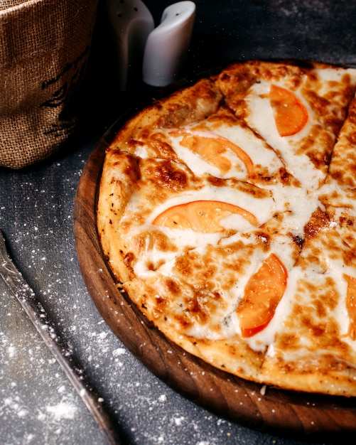 Vista frontal sabrosa pizza con tomates rojos y queso en el piso gris