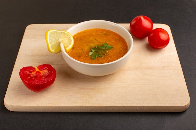 Vista frontal sabrosa sopa de verduras dentro de la placa con rodaja de limón y tomates rojos en el escritorio oscuro.