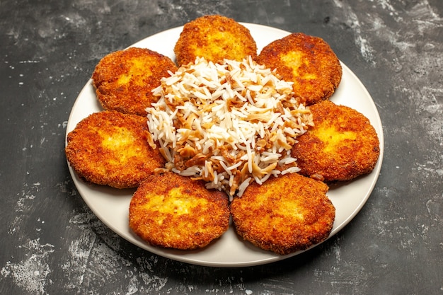 Vista frontal sabrosas chuletas fritas con arroz cocido en superficie oscura foto comida de plato de carne