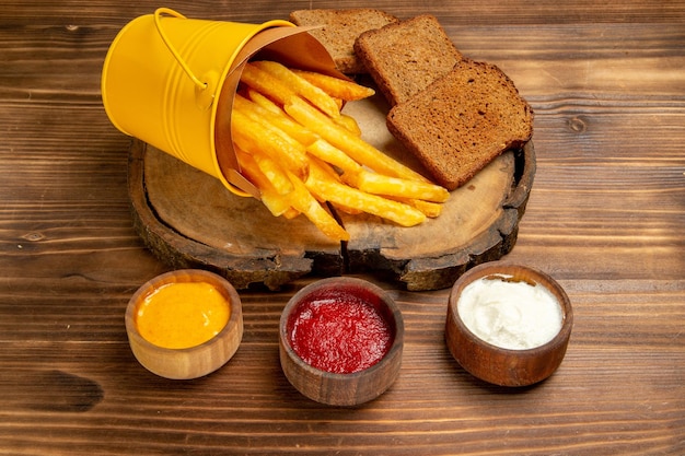 Vista frontal sabrosas papas fritas con condimentos en la comida de pan de comida rápida de papa de escritorio marrón