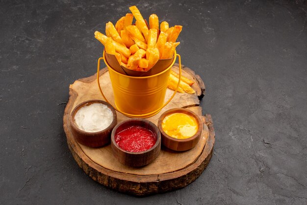 Vista frontal sabrosas papas fritas con salsas en el espacio oscuro