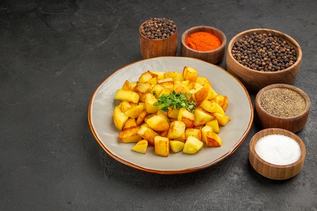 Vista frontal sabrosas patatas fritas dentro de la placa con condimentos en la mesa oscura