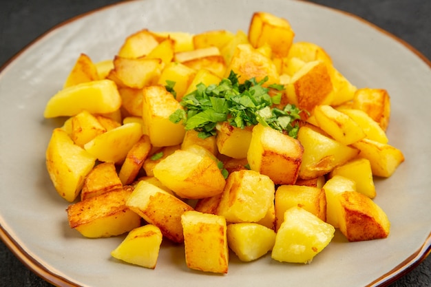 Vista frontal sabrosas patatas fritas dentro de la placa con verduras en la mesa oscura