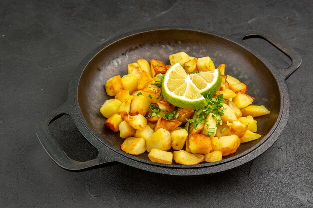 Vista frontal sabrosas patatas fritas dentro de la sartén con limón en la mesa oscura