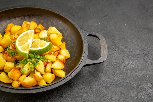 Vista frontal sabrosas patatas fritas dentro de la sartén con rodajas de limón sobre la mesa oscura