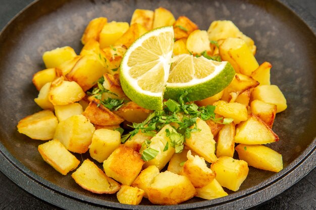 Vista frontal sabrosas patatas fritas dentro de la sartén con rodajas de limón sobre la mesa oscura