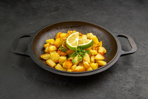 Vista frontal sabrosas patatas fritas dentro de la sartén con rodajas de limón sobre la mesa oscura