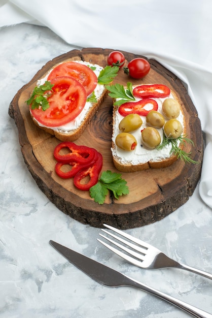 Vista frontal sabrosas tostadas con tomates y aceitunas en tablero de madera blanco