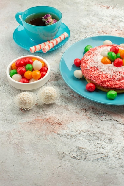 Foto gratuita vista frontal sabroso pastel rosa con caramelos y taza de té sobre fondo blanco pastel de color de postre de caramelo de arco iris de golosinas