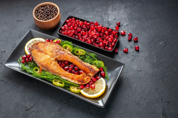 Vista frontal sabroso pescado cocido con granadas y rodajas de limón dentro de la sartén sobre fondo gris oscuro plato color comida foto carne salud mariscos