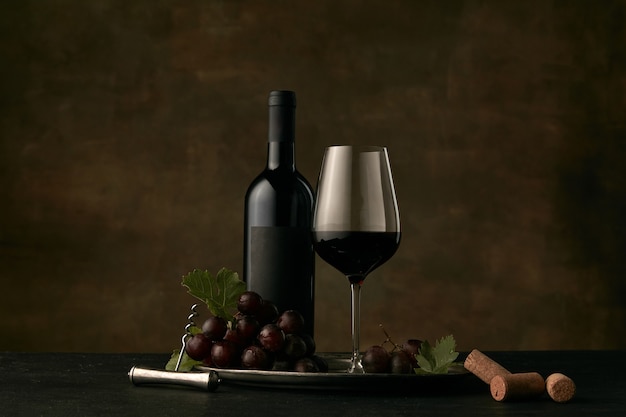 Vista frontal del sabroso plato de frutas de uvas con la botella de vino, queso, frutas y vidrio sobre fondo oscuro