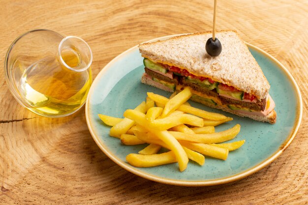 Vista frontal sabroso sándwich con jamón de oliva tomates verduras dentro de la placa con papas fritas y aceite sobre madera