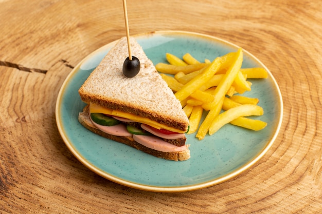 Vista frontal sabroso sándwich con jamón de oliva tomates verduras dentro de un plato con papas fritas en un sándwich de madera bocadillo desayuno