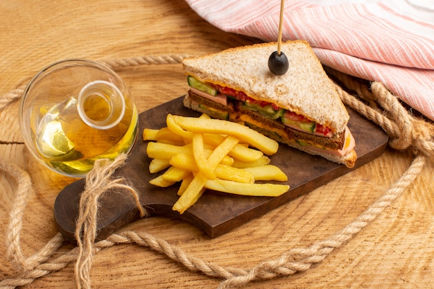 Vista frontal sabroso sándwich con jamón de oliva, tomates, verduras junto con papas fritas, aceite de cuerdas sobre madera