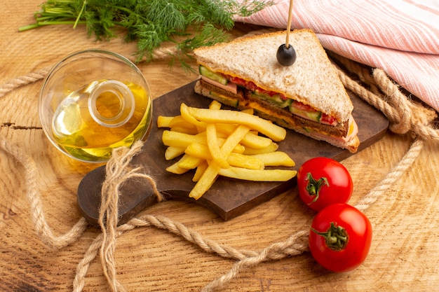 Vista frontal sabroso sándwich con tomates de jamón de oliva junto con papas fritas cuerdas aceite de tomates en madera