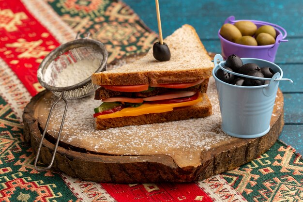 Vista frontal sabroso sándwich de tostadas con jamón de queso en el interior junto con cestas de harina con aceitunas en azul