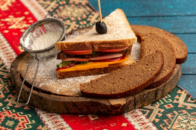 Vista frontal sabroso sándwich de tostadas con jamón de queso en el interior junto con hogazas de pan de harina en azul