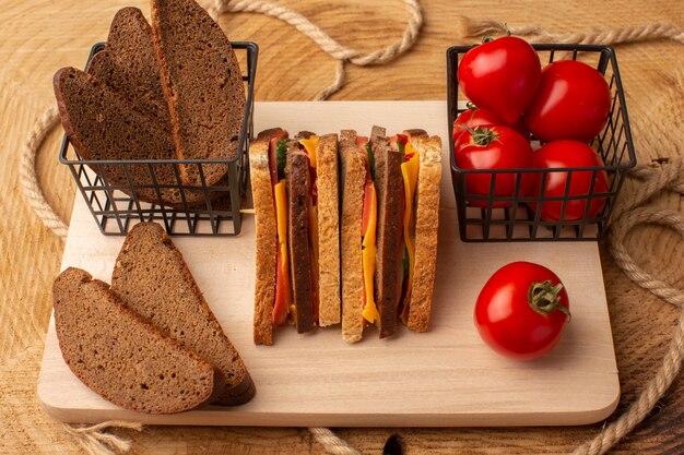 Foto gratuita vista frontal sabroso sándwich de tostadas con jamón de queso junto con panes de pan de tomates rojos en el escritorio de madera