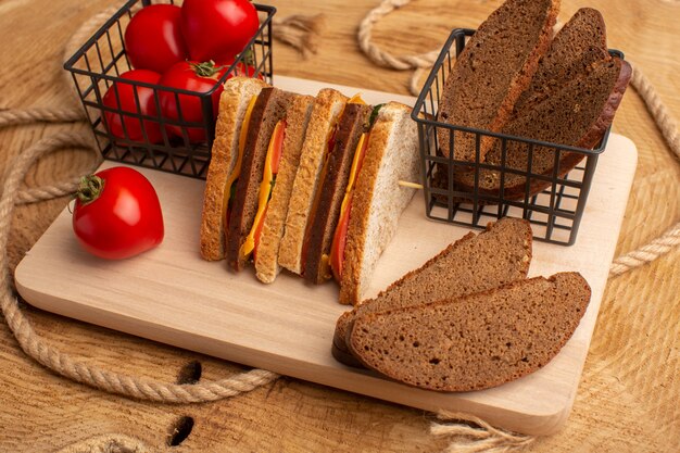 Vista frontal sabroso sándwich de tostadas con jamón de queso junto con panes de pan de tomates rojos en el escritorio de madera