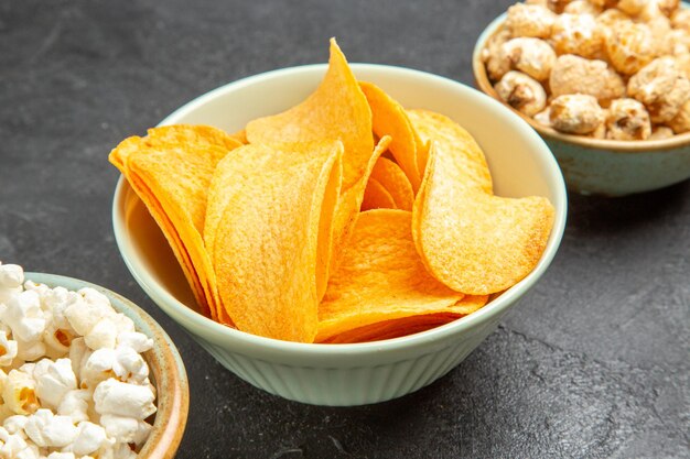 Vista frontal de sabrosos cips de queso con diferentes bocadillos en el piso oscuro