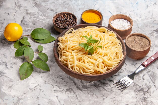 Vista frontal sabrosos espaguetis con condimentos en el plato de pasta de comida de masa de mesa blanca