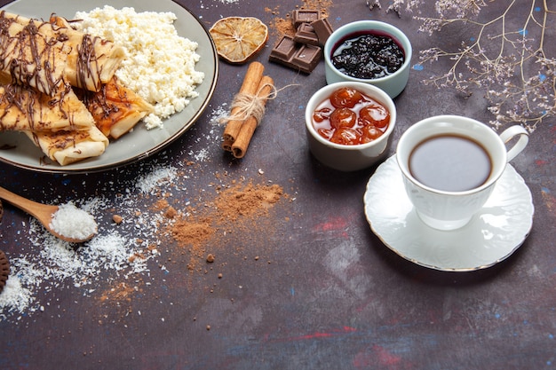 Vista frontal sabrosos pasteles dulces con taza de té y mermelada en el espacio oscuro