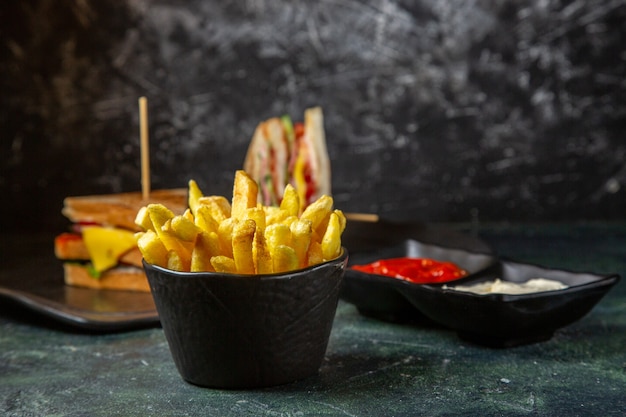 Foto gratuita vista frontal sabrosos sándwiches de jamón con papas fritas comiendo por la superficie oscura femenina